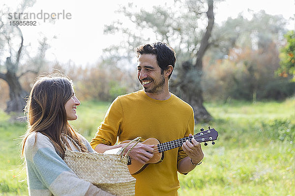 Frau  die einen Weidenkorb trägt  während ein glücklicher Mann auf dem Lande Gitarre spielt