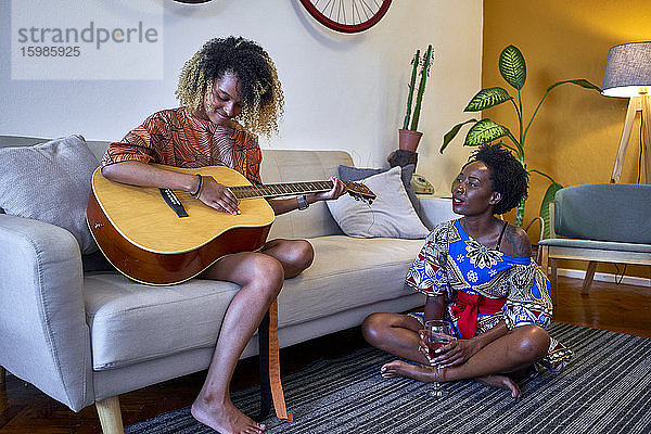 Zwei Frauen mit Gitarre im heimischen Wohnzimmer