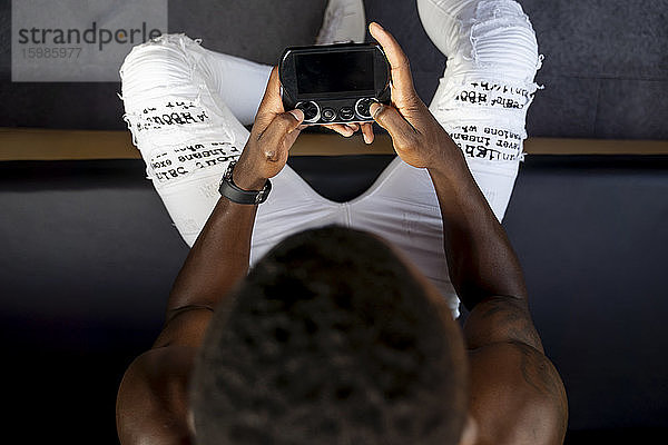 Direkt über der Ansicht eines jungen Mannes ohne Hemd  der ein Handheld-Videospiel spielt