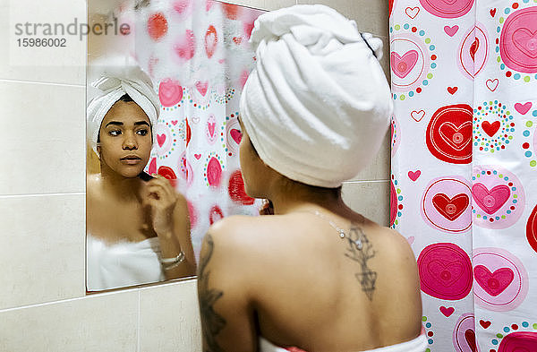 Junge Frau schaut in den Badezimmerspiegel und trägt Make-up auf