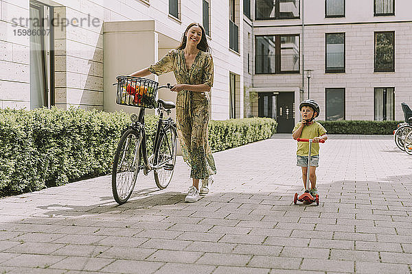 Lächelnde Mutter mit Fahrrad und Sohn mit Motorroller in der Stadt