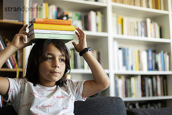 Porträt eines Jungen  der einen Stapel Bücher auf seinem Kopf balanciert