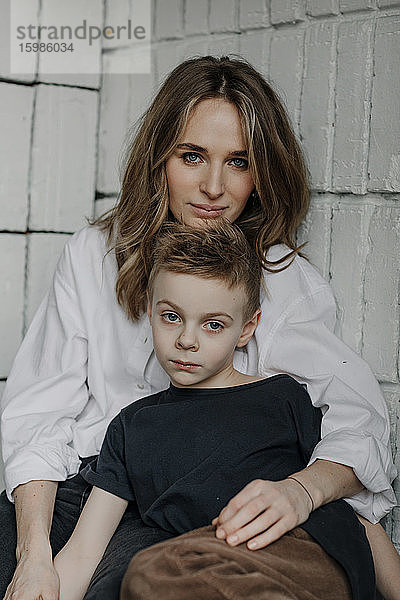 Porträt einer selbstbewussten Frau mit Sohn  die zu Hause auf einer Nische sitzt