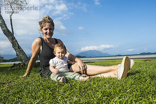 Porträt einer lächelnden Mutter mit ihrer süßen kleinen Tochter auf einer Wiese vor blauem Himmel  Noumea  Neukaledonien