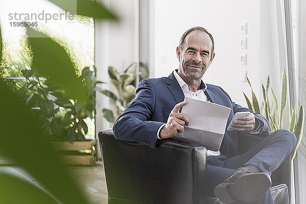 Porträt eines lächelnden Geschäftsmannes mit Smartphone und Dokumenten bei der Arbeit zu Hause
