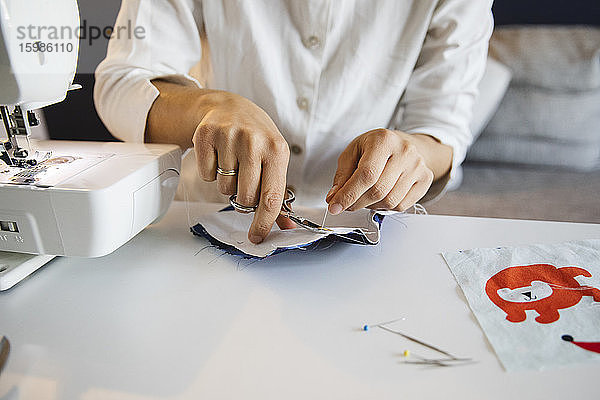 Frau schneidet Faden mit Schere bei der Herstellung einer selbstgemachten Gesichtsmaske