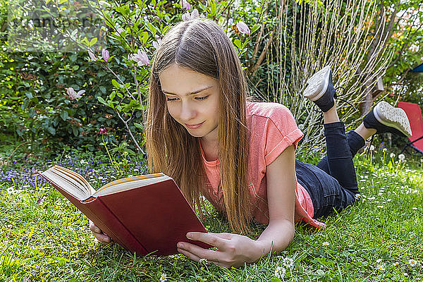 Mädchen liegt auf einer Wiese und liest ein Buch