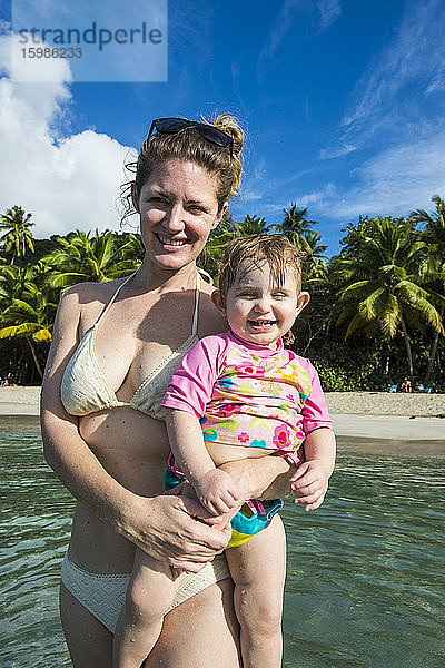 Porträt einer lächelnden Mutter  die ihre süße Tochter im Arm hält  während sie im Meer vor dem Himmel steht  Britische Jungferninseln