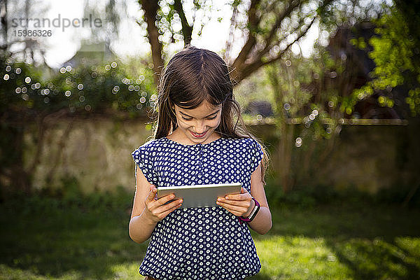 Lächelndes Mädchen  das im Garten steht und ein digitales Tablet benutzt