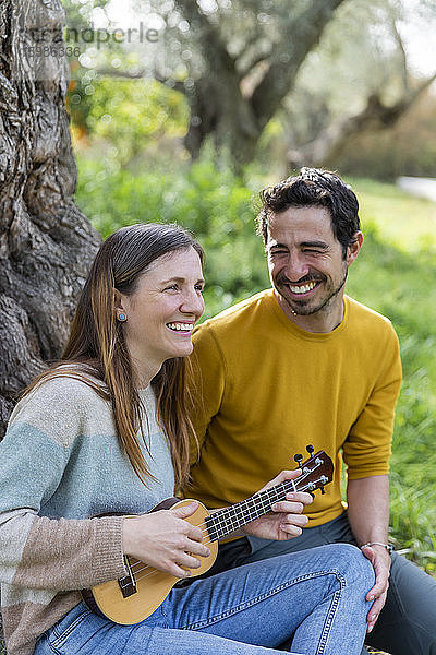 Fröhlicher Mann  der seine Freundin beim Gitarrenspiel beobachtet  während er auf dem Lande sitzt