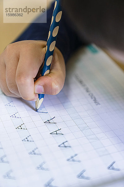 Hand eines Jungen  der zu Hause mit einem Bleistift den Buchstaben A auf Papier schreibt