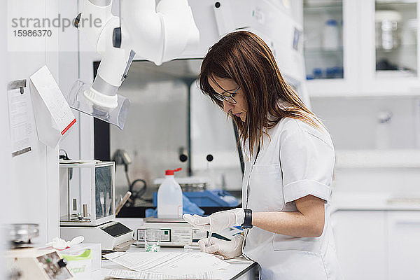 Reife Pharmazeutin hält Tabletten in der Hand  während sie an einem Schreibtisch im Labor steht