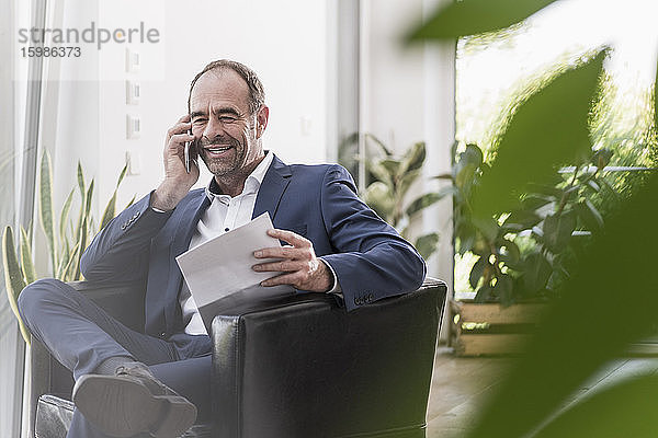 Porträt eines lächelnden Geschäftsmannes mit Dokumenten  der am Telefon spricht
