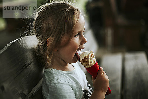 Mädchen isst Eiscreme auf einer Bank sitzend