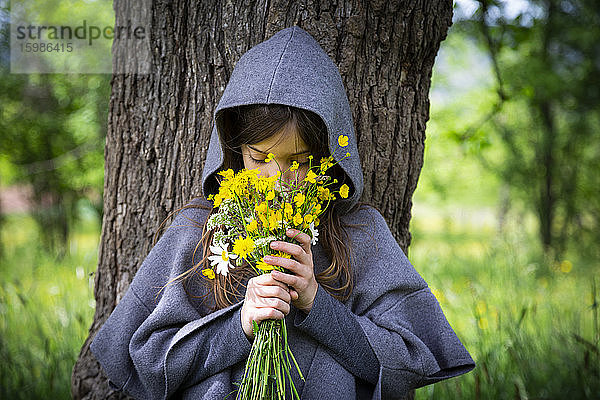 Mädchen riecht an einem Strauß gelber Wildblumen