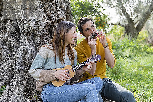 Glückliches Paar spielt Musikinstrumente  während es an einem Baumstamm sitzt