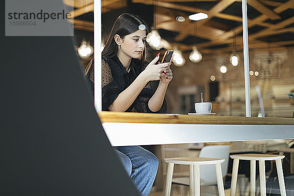 Schöne junge Frau  die ein Mobiltelefon benutzt  während sie in einem beleuchteten Café sitzt