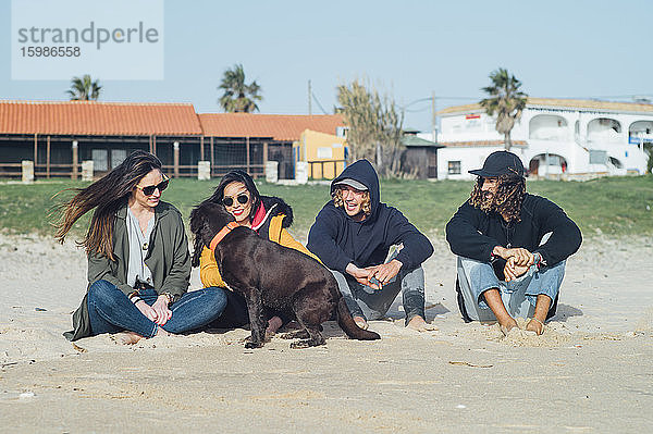 Männliche und weibliche Freunde entspannen sich mit Hund am Strand in Tarifa  Spanien