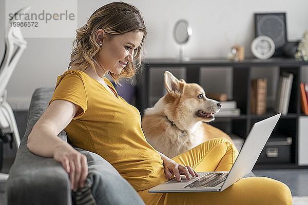 Frau mit Hund benutzt Laptop im Wohnzimmer zu Hause