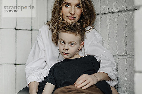 Porträt einer selbstbewussten Mutter mit ihrem Sohn  der zu Hause auf einer Nische sitzt