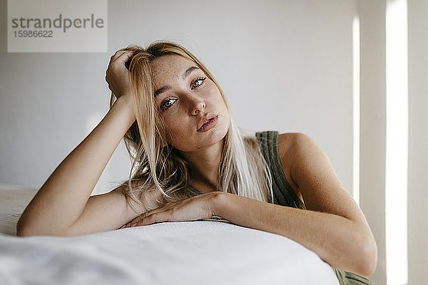 Verführerische junge Frau mit Hand im Haar lehnt Bett zu Hause