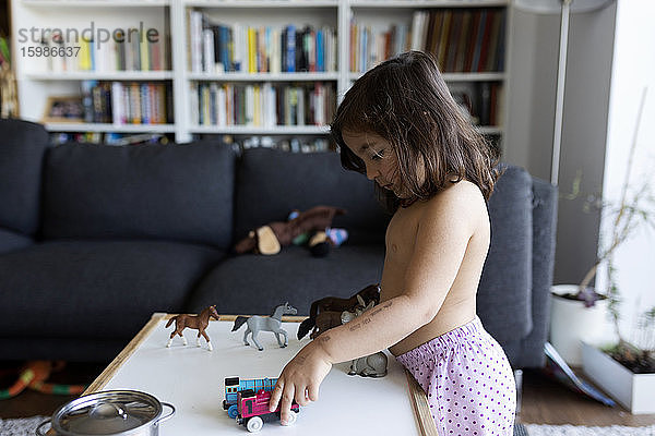 Kleines Mädchen ohne Hemd spielt im Wohnzimmer zu Hause