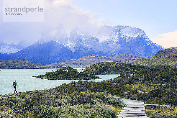 Chile  Provinz Ultima Esperanza  Männlicher Rucksacktourist beim Wandern entlang des Ufers des Pehoe-Sees mit den Cuernos del Paine im Hintergrund