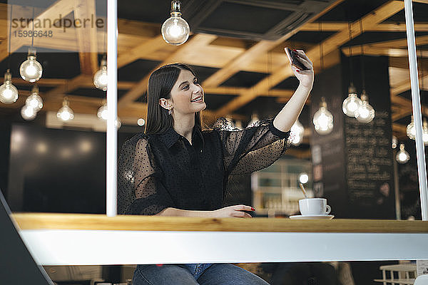 Glückliche junge Frau  die ein Selfie mit ihrem Smartphone macht  während sie in einem Café sitzt