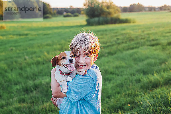 Porträt eines fröhlichen Jungen mit Hund auf einem Feld an einem sonnigen Tag  Polen