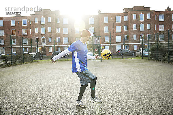 Älterer Mann spielt mit Fußball auf einem Fußballplatz in der Stadt