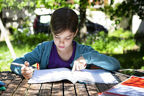 Mädchen sitzt am Gartentisch und macht Hausaufgaben