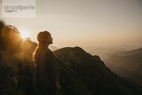 Lächelnder junger Wanderer bei der Erkundung eines Berges gegen den Himmel bei Sonnenuntergang  Sri Lanka