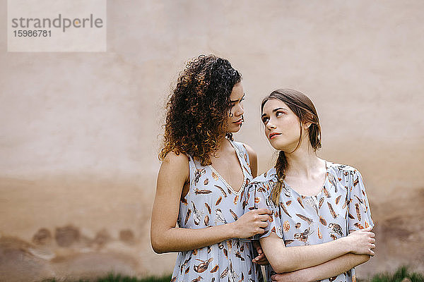 Verliebte Schwestern in Kleidern  die sich gegenseitig anschauen  während sie an einer alten Wand stehen