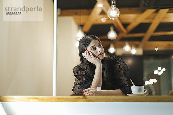 Nachdenkliche junge Frau sitzt am Tisch in einem beleuchteten Café