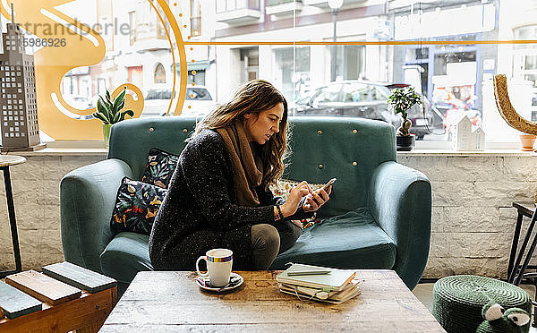 Frau mit Smartphone auf der Couch in einem Café sitzend