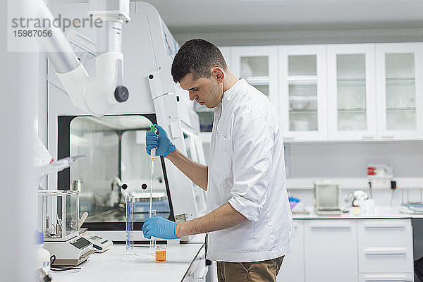 Junger männlicher Wissenschaftler  der eine Chemikalie mit einer Pipette aufnimmt  während er im Labor forscht