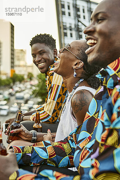 Lachende Freunde sitzen auf einer Dachterrasse in der Stadt und trinken Bier  Maputo  Mosambik