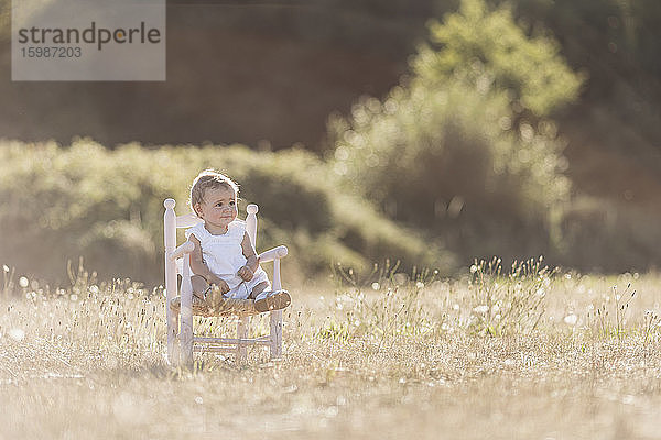 Nettes Kleinkind Mädchen sitzt auf Stuhl auf Wiese während sonnigen Tag