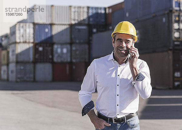Porträt eines lächelnden Geschäftsmannes am Telefon vor einem Frachtcontainer