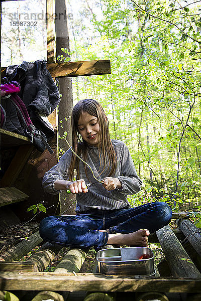 Mädchen schnitzt ein Stück Holz  das auf einem Hochsitz im Wald sitzt