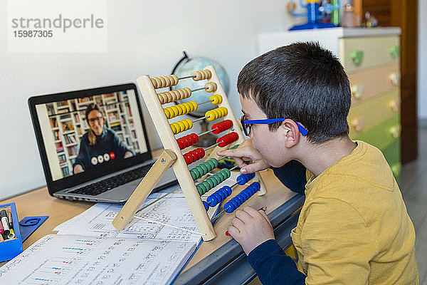 Junge mit Abakus am Schreibtisch  während der Lehrer per Videoanruf während der Pandemie Hausunterricht erteilt