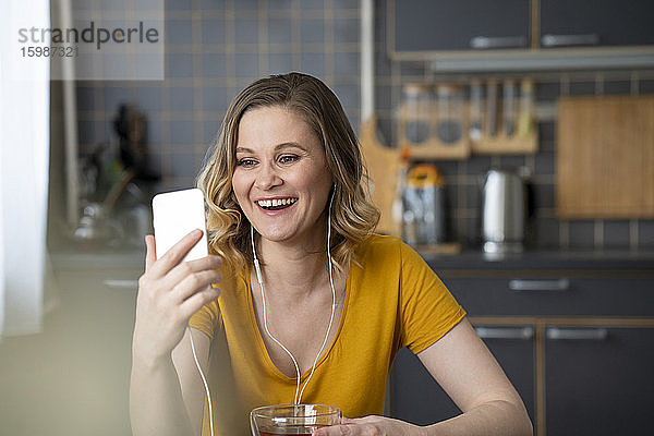 Glückliche Frau  die in der Küche zu Hause einen Videochat mit ihrem Smartphone führt