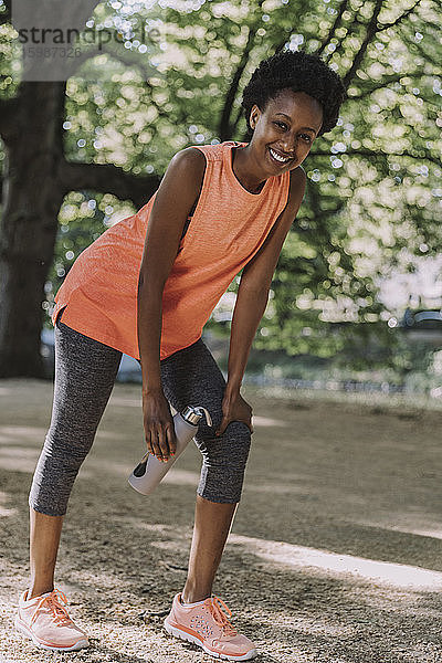 Porträt einer lächelnden jungen Frau  die eine Pause vom Training in einem Park macht