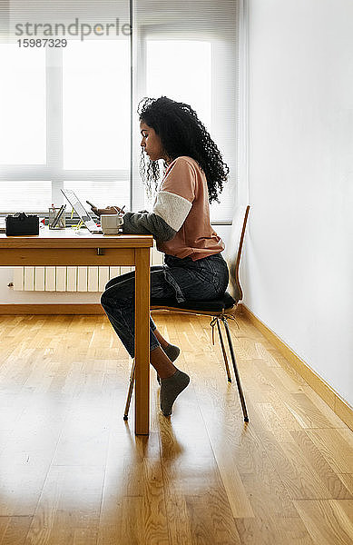 Junge Frau arbeitet von zu Hause aus mit Laptop und Smartphone