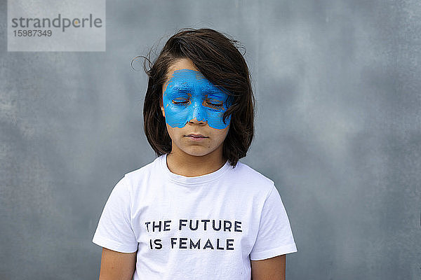 Porträt eines Jungen mit aufgemalter blauer Maske im Gesicht  der ein T-Shirt mit dem Aufdruck 'The Future is Female' trägt