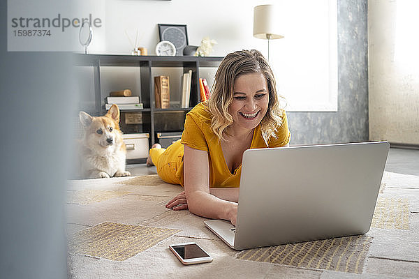 Glückliche Frau mit Hund  die einen Laptop im Wohnzimmer zu Hause benutzt
