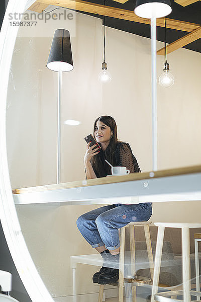 In voller Länge der schönen Frau sitzt mit Smartphone und Kaffee im Cafe