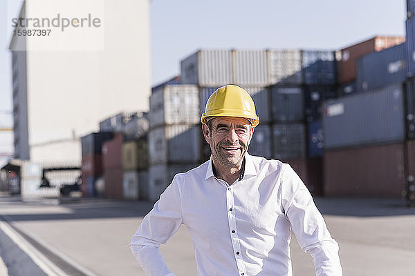 Porträt eines lächelnden Geschäftsmannes mit Schutzhelm vor einem Frachtcontainer