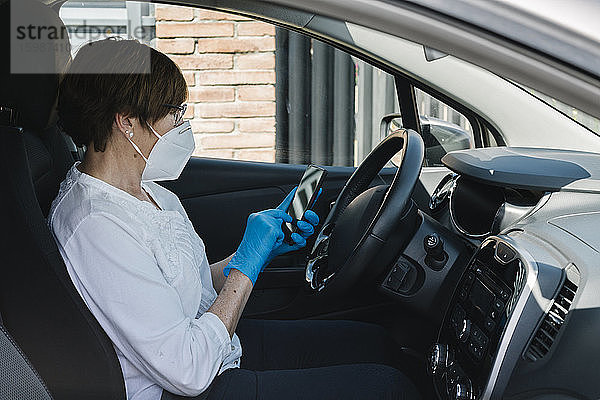 Frau mit Maske im Auto benutzt Smartphone