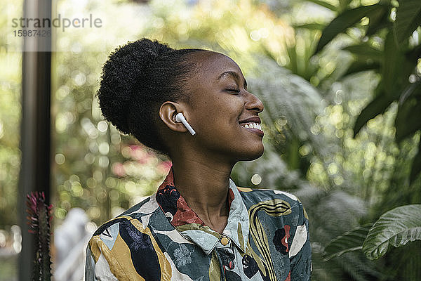 Glückliche junge Frau mit geschlossenen Augen hört Musik mit Kopfhörern im Garten